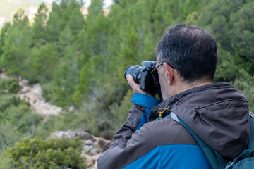 Man with backpack and slr camera takes photos to the landscape in the morning
