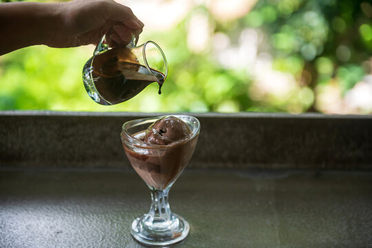 Affogato hot fudge pouring by man hand over chocolate ice cream