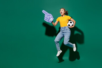 Fototapeta na wymiar Full body young woman fan in yellow t-shirt foam 1 glove finger up point overhead cheer up support football sport team hold in hand soccer ball watch tv live stream isolated on dark green background