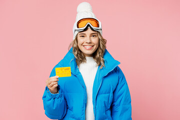Snowboarder woman fun wear blue suit goggles mask hat ski padded jacket hold mock up of credit bank card isolated on plain pastel pink background Winter extreme sport hobby weekend trip relax concept