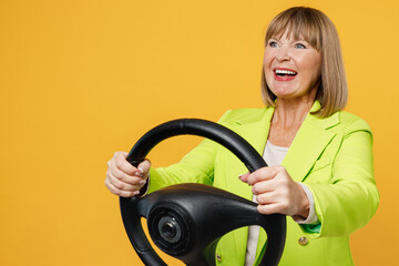 Side view elderly happy woman 50s years old wear green jacket white t-shirt hold steering wheel driving car look camera isolated on plain yellow background studio portrait. People lifestyle concept