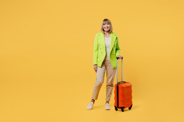Full body elderly woman 50s years old wearing green jacket white t-shirt hold valise isolated on plain yellow background Tourist travel abroad in free spare time rest. Air flight trip journey concept