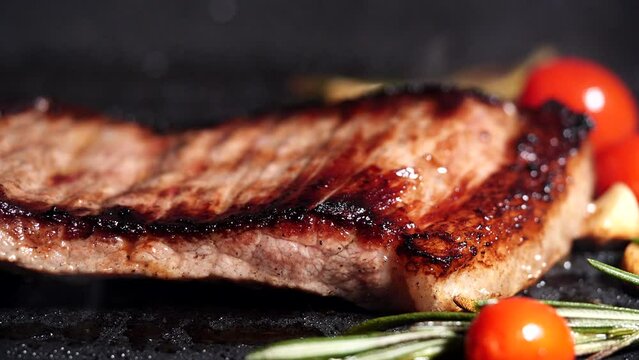 Grilling beef steak, meat steak with rosemary, tomatoes, garlic on hot iron plate. Concept of Grill Beef Meat Steak