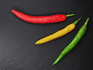 three different colored chili peppers on black slate background, top view of red, yellow and green...