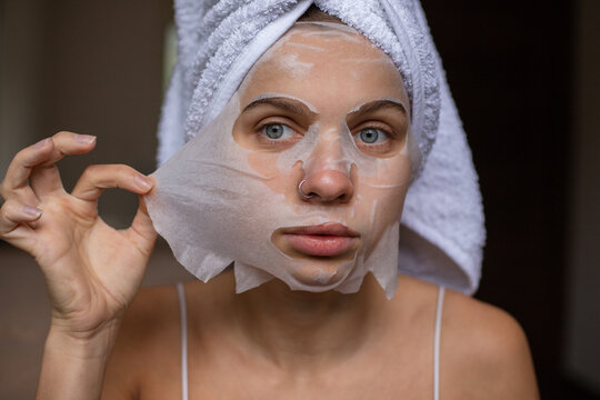 Beauty portrait woman with a towel wrapped around her head taking off sheet mask