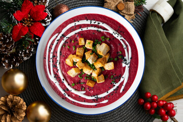 Beetroot soup with toasted bread croutons and cream on a table with Christmas decorations.