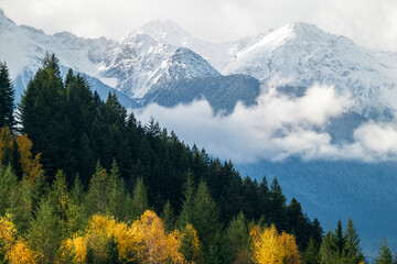 Panorama photo with mountain peaks and low hanging clouds with fall colors in Canadian Rockies