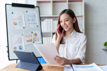 Asian businesswoman sitting happily working on a laptop and talk on the phone to contact customers, talk to explain the job and smile happily.