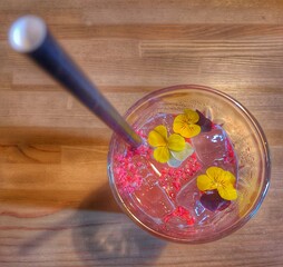 Summer cocktail, non-alcoholic rhubarb drink, decorated with edible flowers. A glass with a straw. Drink with ice cubes.