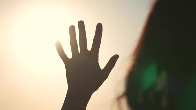Silhouette of happy dreaming girl pulls her hand to the sun. Religion helping hand. Happy girl pulls her hand. Prayer in religion. Silhouette of hand in the sun. Happy girl silhouette at sunset