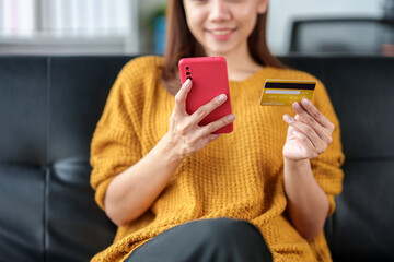 Lovely and bright Asian businesswoman conveniently shopping online on mobile using credit card for the convenience of spending at home on vacation.