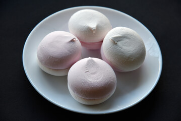 Pink and white marshmallows on a white plate on a black background. Delicious sweet snack on a plate. Marshmallow close-up.