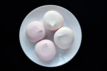 Pink and white marshmallows on a white plate on a black background. Delicious sweet snack on a plate. Marshmallow close-up.