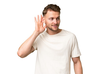 Fototapeta premium Young blonde caucasian man over isolated background listening to something by putting hand on the ear