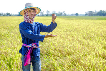 Naklejka na ściany i meble Thai male farmer in traditional dress and headdress standing pose holding goods smiling in the middle of the field
