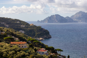 Fototapeta na wymiar Residential Homes on Mountain by the Sea with Capri Island in background. Near Touristic Town of Sorrento, Italy.