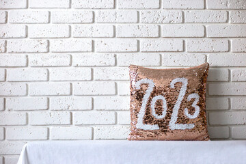 Golden pillow  with paillettes with inscription 2023. Pillow with sequins on brick wall background....