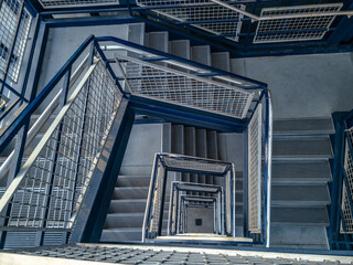 Stairwell in a parking garage. The steps in the stairwell are made of concrete and the hand railings are metallic and painted blue. Located at the big blue deck at the Detroit Metro Airport in Romulus