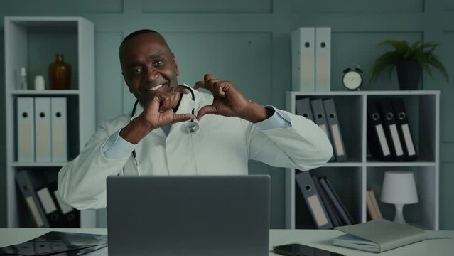 Kind peaceful caring medical worker mature african american man cardiologist doctor in white coat shows heart love shape at camera health care charity support for patients checkup cardiology diseases