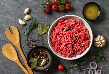 Plate of minced beef meat with vegetables and spices on dark background with copy space top view. Fresh raw ingredients for cooking healthy food. Preparation background