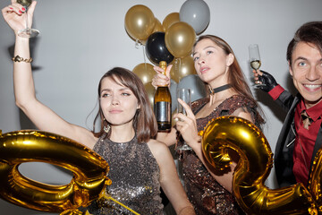 Two girls and man in stylish outfits having great New Year party with alcohol drinks 