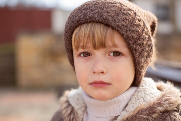 a large portrait of a sad little boy with big brown eyes in a knitted hat