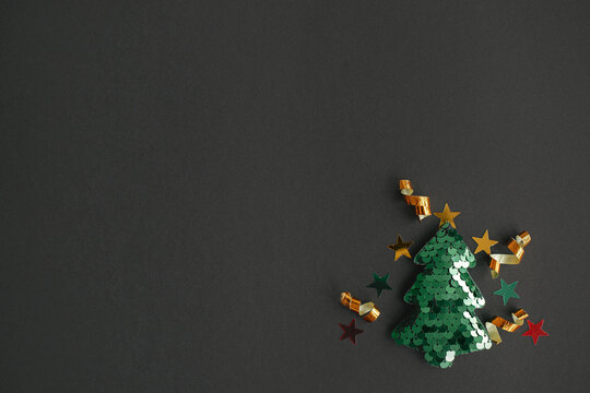 Christmas tree modern minimal flat lay, winter holidays concept. Stylish little christmas tree with sparkling gold confetti on black background. Merry Christmas! Space for text. Creative idea
