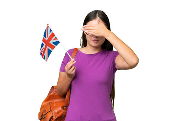 Young Asian woman holding an United Kingdom flag over isolated background covering eyes by hands. Do not want to see something