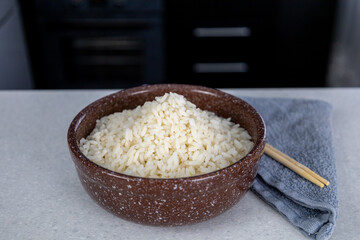 A plate of brown color with golden rice on the table against the backdrop of a dark kitchen. Chopsticks lie next to the towel. Asian food concept