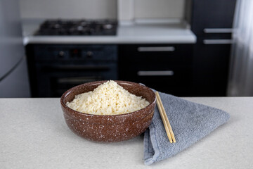A plate of brown color with golden rice on the table against the backdrop of a dark kitchen. Chopsticks lie next to the towel. Asian food concept