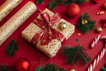 Modern christmas composition. Stylish christmas gift, wrapping paper,  fir branches, candy cane and baubles on red background. Merry Christmas and Happy Holidays! Festive banner