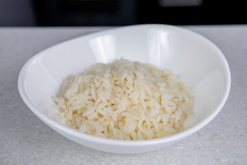 A white oriental plate with golden rice stands on a table in a dark kitchen. Asian food concept
