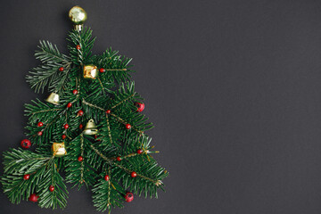 Christmas tree, winter holidays concept. Stylish christmas tree made of fir branches, red berries and gold baubles on black background, flat lay. Creative idea. Modern festive banner