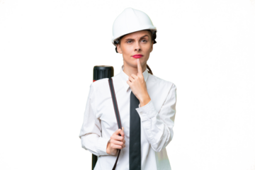 Young architect woman with helmet and holding blueprints over isolated background having doubts