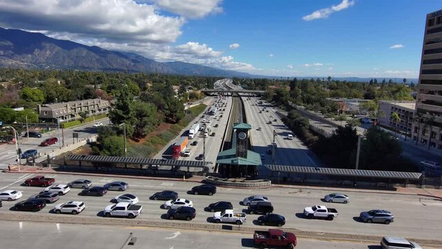 aerial footage of the clock tower at the Lake Avenue overpass of the 210 Freeway with cars and trucks driving surrounded by lush green trees, buildings, and mountains in Pasadena California USA