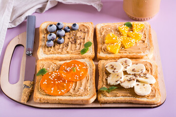 Toast with peanut butter, banana, persimmon, orange, flax seeds and sesame seeds on a cutting board.