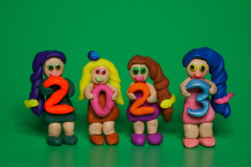 Figurines of girls made of plasticine and the figure 2023. A festive event. Calendar date. Green background.