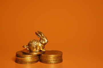 Fototapeta na wymiar A metal rabbit figurine with coins on a bright background. Financial symbol. The year of the rabbit.
