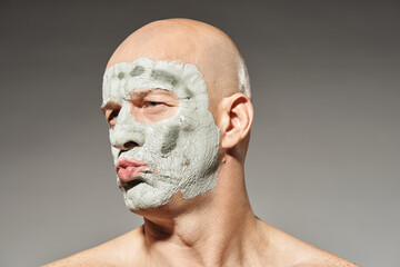 Beauty portrait of playful adult man with dry clay mask making duck face looking away 