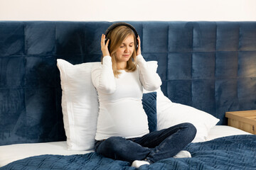 Beautiful pregnant woman with big belly wears headphones, sitting on bed, prenatal hypnosis, music...
