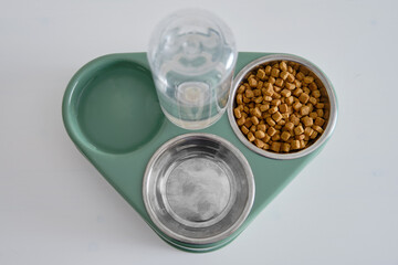 A bowl of dry cat food on a white background . Green triple plate with water for a pet, close-up