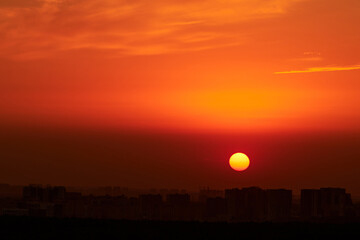 A big red sun in the sunset sky over the roofs of buildings, urban landscape. Evening sky in bright sunlight over the twilight city