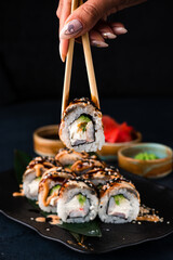 Japanese sushi rolls with smoked eel, shrimps, cream cheese, avocado and chopsticks in a woman's hand.