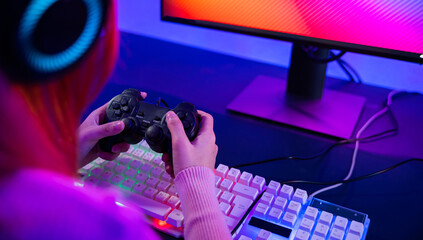 Gamer using joystick controller for virtual tournament plays online video game with computer neon lights, woman wear gaming headphones playing live stream esports games console at home © sorapop