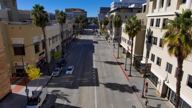 aerial footage along Colorado Blvd with cars driving along the street and people walking on the sidewalk lined with lush green palm trees and buildings in Pasadena California USA