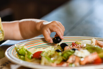 Baby hand take big olive from salad