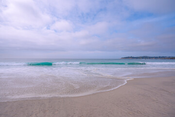 Light airly seascape in blue and pink colors. Wide sandy beach, sea waves, and cloudy sky