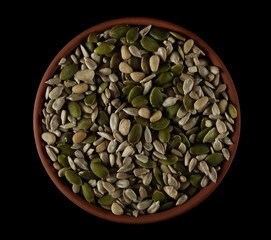 Mix seed, pumpkin seeds, sunflower seeds and pine nuts in clay pot isolated on black, top view