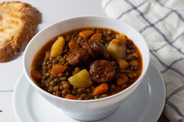 Traditional lentil soup with legs, carrots and chorizo on a white on a white background. Mediterranean cuisine.