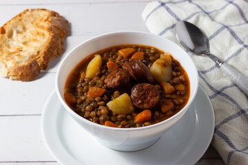 Traditional lentil soup with legs, carrots and chorizo on a white on a white background. Mediterranean cuisine.